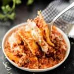 a white bowl filled with pasta and sauce on top of a table next to a fork