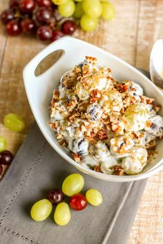 a bowl filled with grapes and nuts on top of a table next to some fruit