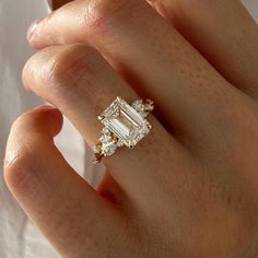 a woman's hand wearing a ring with an emerald and yellow diamond in it