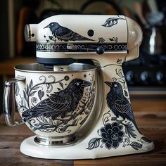 two black birds are sitting on top of a white stand mixer that is decorated with flowers and leaves