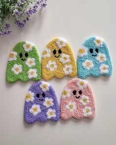 four crocheted mittens with flowers and smiley faces on them, sitting next to a plant