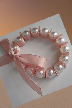 a pink ribbon and pearls bracelet on top of a piece of paper with a bow