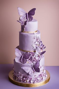 a three tiered cake with purple butterflies on the top and gold trimmings