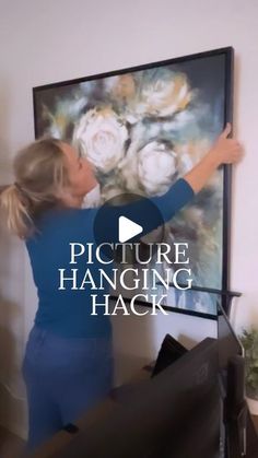 a woman standing in front of a large painting with the words picture hanging hack on it