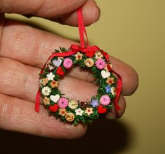 a hand holding a small wreath ornament with flowers and hearts on it's side