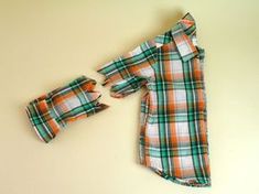 an orange and green plaid shirt laying on top of a white table next to a pair of scissors