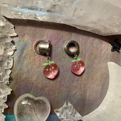 two pink heart shaped earrings sitting on top of a piece of glass next to ice crystals