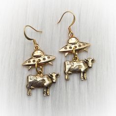 "Cute golden cows being abducted by UFO/ Aliens.  Gold plated zinc alloy and pewter cow charms, on your choice of gold plated brass ear hooks. Approx 4 grams each, and  1.75\" long. Sold per pair (leave listing qty as 1) * Fish hook * Lever back * Kidney (47mm, will fit through stretched ear tunnels) * Star shaped Post-style * Clip on (non-piercing)  * 14K Gold-Filled Fish hooks (Please note there are no star charms included on the fishhook/leverback/kidney styles, only the star-shaped post style) : V I E W   S H O P:.. www.lotusfairy.etsy.com www.shopEarthshine.com ..: P O L I C I E S :.. Please see the drop down FAQs menu All items are FINAL SALE. ★ I M P O R T A N T ★ This product is not intended to be used by, or around,  anyone under the age of 13.  ShopEarthshine.com ★ lotusfairy.ets Cow Earrings, Lavender Moon, Stretched Ear, Ear Tunnels, Fish Hooks, Moon Ring, Funky Jewelry, Cute Little Things, Jewelry Inspo