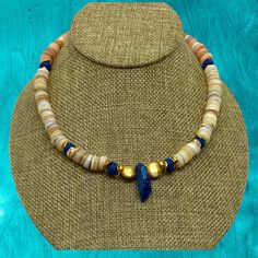 Experience the tropical vibes with our stunning 17" Fiji Choker Necklace of Lapis Lazuli, Gold, and beach-colored shells and beads. From the glint of gold to the mesmerizing blue of the Lapis Lazuli, this exquisite piece will make you feel like you've escaped to an island paradise! Toggle style closure. Unisexy! Gold Spiritual Jewelry For Vacation, Beach Jewelry With Gemstone Shell Beads, Shell Jewelry With Gemstone Beads For Beach, Bohemian Single Strand Shell Necklace For Beach, Gold Beaded Shell, Adjustable Polished Beads Necklace For Beach, Adjustable Polished Bead Necklaces For Beach, Adjustable Gold Beaded Shell Necklace, Ocean-inspired Gold Jewelry With Natural Stones