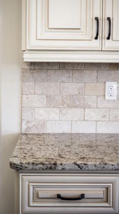 a kitchen counter top with white cabinets and marble tile backsplash in the background