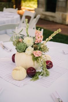 a vase filled with flowers and fruit sitting on top of a white tablecloth covered table