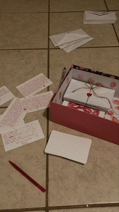 an open box sitting on top of a tiled floor next to papers and pencils