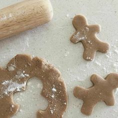 three gingerbread cookies with icing on a white surface next to a rolling pin