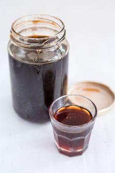 there is a small glass cup with liquid in it next to a jar full of syrup