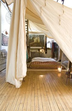 a bed sitting inside of a white tent on top of a wooden floor next to a window