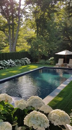 a pool surrounded by lush green grass and white hydrangeas in the foreground