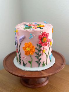 a pink cake decorated with flowers and butterflies on a wooden platter next to a white wall