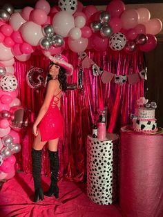 a woman in a pink dress and hat posing for the camera with balloons behind her