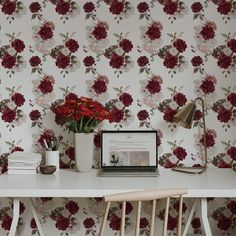 a laptop computer sitting on top of a white desk next to a flower covered wall