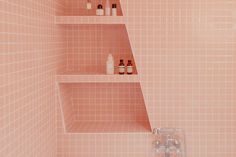 a pink tiled bathroom with shelves and soap bottles on the bathtub, along with toiletries