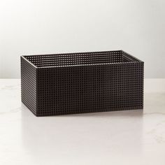 a black basket sitting on top of a white counter next to a planter with holes in it