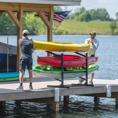 two men standing on a dock with kayaks and an american flag in the background