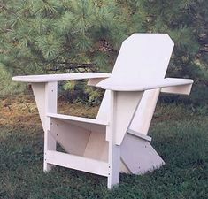 a white chair sitting on top of a grass covered field next to a pine tree