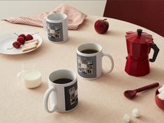 two coffee mugs sitting on top of a table next to a plate of food