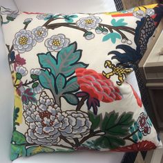 a close up of a pillow on a bed with colorful flowers and birds in the background