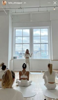 a group of women sitting on top of yoga mats in front of a large window