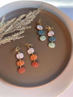 three earrings are sitting on a plate next to a plant and some dried grass in the background