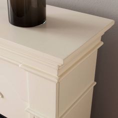 a black candle is sitting on top of a white dresser with drawers and knobs