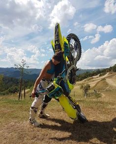 a man holding onto his bike while standing on top of a dirt field with mountains in the background