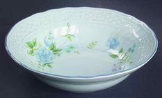 a white bowl with blue flowers and green leaves on the rim is sitting on a black surface