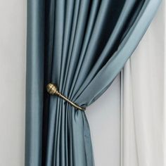 an open curtain with a gold handle attached to it's side in front of a white wall