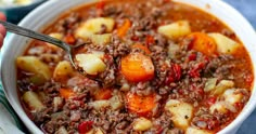 a person holding a spoon over a bowl filled with stew, potatoes and carrots