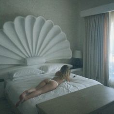 a woman laying on top of a bed next to a large white shell headboard