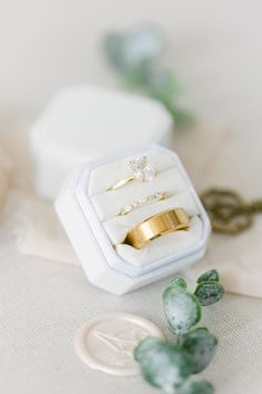 two gold wedding rings sitting in a white ring box next to a green plant and key