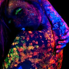 a woman covered in holographic paint holding a teddy bear with her arms wrapped around her body