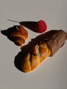 two croissants wrapped in brown paper next to a strawberries on a white surface