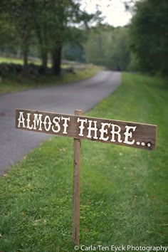 a wooden sign sitting on the side of a road next to a lush green field