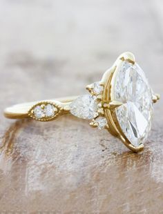 a yellow gold engagement ring with three pear shaped diamonds on the side and an oval cut diamond in the middle