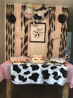 a cow themed dessert table with cupcakes and cake on the table in front of it