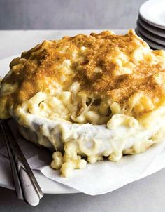 a white plate topped with macaroni and cheese covered in gravy next to silverware