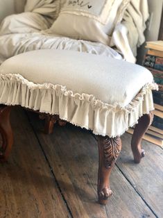 a white bench with ruffled edges on a wooden floor in front of a bed