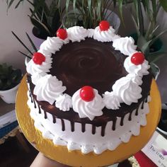 a chocolate cake with white frosting and cherries on top sitting on a table