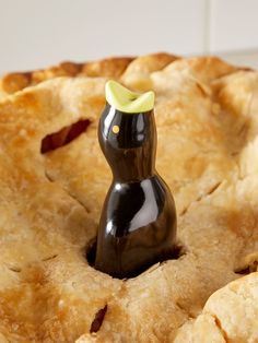 a small black cat figurine sitting in the middle of a baked pie crust