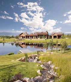 a large house sitting on top of a lush green field next to a lake and forest