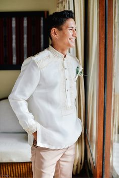 a man standing in front of a window wearing a white shirt and khaki pants