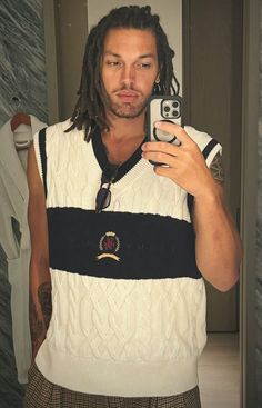 a man with dreadlocks taking a selfie in front of a mirror wearing a sweater vest